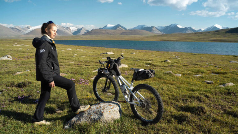 kate leeming standing with her bike on some grass next to a river